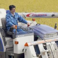 Prime Minister Shinzo Abe tries his hand at running a rice harvester in Hirono, Fukushima Prefecture, on Wednesday. | POOL
