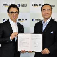 Amazon Japan President Jesper Cheung (left) and Tokushima Gov. Kamon Iizumi show off an agreement signed Friday between the online retailer and the Tokushima Prefectural Government at the prefectural office in the city of Tokushima. The agreement will allow people to buy and donate disaster relief goods through the company\'s website if the prefecture is hit by a natural disaster. | KYODO
