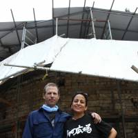 Married sculptors Steven Ward and Ximena Elgueda have spent the past 14 years building a terra-cotta amphitheater for the performing arts. They are seen in front of a kiln erected to bake the stage\'s ceramic rear wall, which directs sound at the audience. | CHUNICHI SHIMBUN