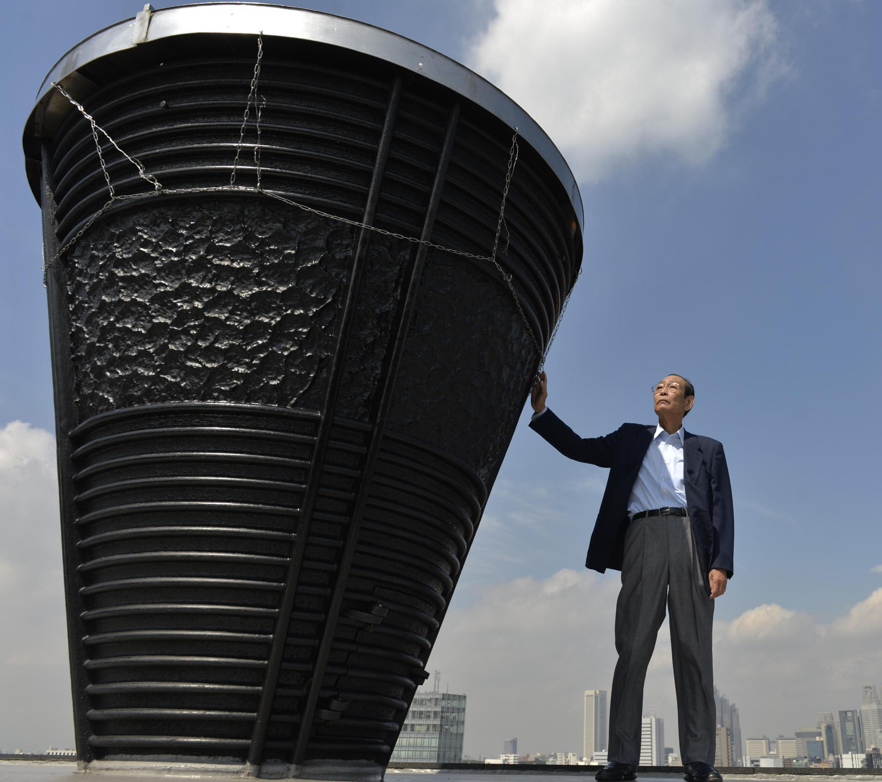 Yoshinori Sakai, who ran the final leg of the torch relay for the 1964 Tokyo Olympics, touches the base of the Olympic torch at National Stadium in Shinjuku Ward in September 2013. | KYODO