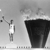 Yoshinori Sakai, who ran the final leg of the torch relay for the 1964 Tokyo Olympics, lights the Olympic torch at National Stadium in Shinjuku Ward in October 1964. | KYODO