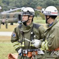Two fire department workers stand in front of a Ground Self-Defense Force helicopter on Tuesday morning in the village of Otaki, Nagano Prefecture, after rescue operations were halted on Mount Ontake due to dangers from volcanic tremors and fumes. | KYODO