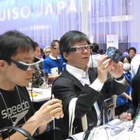 Visitors at the CEATEC trade show Tuesday try out Seiko Epson Corp.\'s Moverio smart glasses, which can display video. | KAZUAKI NAGATA