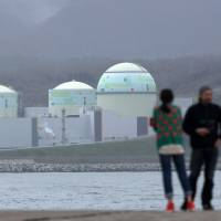 A couple stand in front of Hokkaido Electric Power Co.’s nuclear power plant in the village of Tomari in May 2012. Hokkaido Electric wins government OK to raise rates