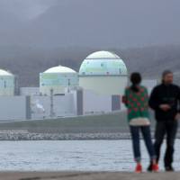 A couple stand in front of Hokkaido Electric Power Co.\'s nuclear power plant in the village of Tomari in May 2012. | BLOOMBERG