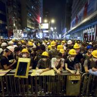Protesters stand guard behind a barricade at the occupied area in the Mong Kok district of Hong Kong early Monday. Three weeks ago, students at a rally stormed a fenced-off courtyard outside Hong Kong\'s government headquarters, triggering unprecedented mass protests for greater democracy in the semiautonomous Chinese city. | AP