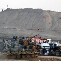 Turkish forces on the outskirts of Suruc secure the border with Syria as militants with the Islamic State group are seen after placing their group\'s flag on a hilltop at the eastern side of the town of Kobani, Syria (background), where fighting intensified Monday between Syrian Kurds and the jihadists. | AP