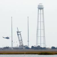 A helicopter does reconnaissance over the launchpad at NASA Wallops Flight Facility on Wednesday, when authorities started investigating what made the 14-story Antares rocket, an unmanned U.S. supply rocket built and launched by Orbital Sciences Corp., explode in a fireball moments after lifting off from the launchpad, destroying supplies and equipment bound for the International Space Station. | REUTERS