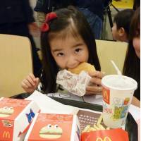 A girl bites into a hamburger Wednesday at a McDonald\'s in Tokyo\'s Odaiba district with a set meal featuring the \"Yokai Watch\" anime series. | KYODO