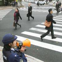 A police officer calls on passers-by to follow traffic rules at a crossing in Morioka, Iwate Prefecture, during a competition on Wednesday to guide pedestrians and cars safely. | KYODO