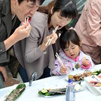 Parents and a child tuck into some grilled saury at the annual Meguro \"sanma\" festival on Sept. 7. | YOSHIAKI MIURA