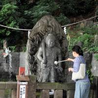 A woman pours water before a statue of the god of fire at Meguro Fudo Temple on Sept. 17. | YOSHIAKI MIURA