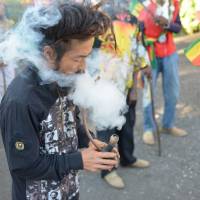 A Japanese Rastafarian named Bongho Jatusy puffs on a ganja pipe outside a museum dedicated to Marley, also in the Jamaican capital. | AP