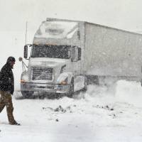 A truck driver walks in front of his tractor-trailer Tuesday after it got stuck on an off ramp outside Boston, New York. Parts of New York measured the season\'s first big snowfall on Tuesday as 3 feet (about a meter) of lake-effect snow blanketed the Buffalo area. | AP