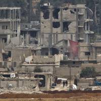Armed people, believed to be Kurdish fighters, walk between damaged buildings in the Syrian city of Kobani, as seen from a hilltop outside Suruc, on the Turkey-Syria border Monday. Kobani has been under assault by extremists of the Islamic State group since mid-September and is being defended by Kurdish fighters. | AP