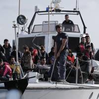 A Greek coast guard officer stands next to a small group of immigrants on a launch carrying them to shore from a crippled smuggling ship with more than 700 people, at the coastal Cretan port of Ierapetra, Greece, on Thursday. The ship, whose passengers are mostly Syrians, including children, women and elderly men, suffered engine failure 70 nautical miles off Ierapetra on Tuesday. The migrants will be given temporary shelter at an Ierapetra indoor basketball stadium. For 700 migrants, harrowing sail ends in Greece