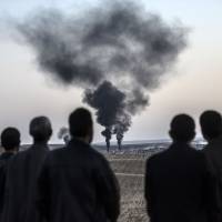 Men gathered near the southeastern Turkish border village of Mursitpinar watch as smokes rises from the Syrian town of Kobani following coalition airstrikes against Islamic State group militants on Oct. 26, . | AFP