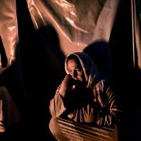 Syrian Kurdish refugees sit outside a tent Tuesday at a refugee camp in Suruc in Turkey\'s Sanliurfa province.  The U.N. says more than 13 million people displaced by the wars in Iraq and Syria are facing a harsh winter. | AFP-JIJI