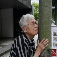 Asayo Sakai, a dementia patient, rubs her face against a tree while saying \"Thank you\" as she waits for a car to take her to a day care center in Osaka. | BLOOMBERG