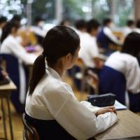 Students attend a class at the Korean High School in Kita Ward, Tokyo, on Sept. 25. The school looks much like a Japanese educational institution, with a large clock sitting atop of gray buildings. Inside, all notices are written in Korean and female students and teachers wear the traditional \"chima jeogori,\" a full skirt and short jacket. | BLOOMBERG