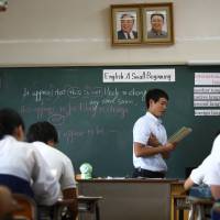 Portraits of the late North Korean leaders Kim Il Sung (left) and Kim Jong Il are displayed in a classroom as a teacher conducts an English class at the Korean High School in Tokyo on Sept. 25. | BLOOMBERG