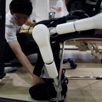 A Cyberdyne Inc. employee adjusts a Lower Limb Model HAL (Hybrid Assistive Limb) during a training session in Tsukuba, Ibaraki Prefecture, on July 22. The device can help people such as stroke victims who have partial paralysis. | REUTERS