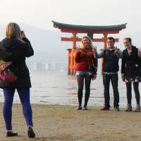 Foreign tourists take a photo at Itsukushima Shrine in Hiroshima Prefecture, which is designated as a UNESCO World Heritage site, in February. | KYODO