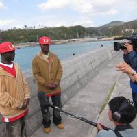 Local interest: Ugandan singers Musa Jian (left) and Baswali Kiramu speak to Okinawan media at Teima fishing port in Henoko. | JANE CLOSE