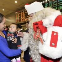 An officially registered Finnish Santa Claus who arrived in Japan on Friday hands a piece of chocolate to a mother and her baby at Narita International Airport. He is expected to travel to various parts of the country until Christmas Eve. | KYODO
