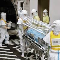 Health workers in protective suits wheel an actor portraying a suspected Ebola patient on a stretcher during a drill Monday in Izumisano, Osaka Prefecture. The exercise was held in the event that a flight carrying passengers suspected of being infected with the deadly virus arrives at nearby Kansai International Airport.  | KYODO