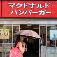 A woman walks past a McDonald\'s restaurant in Tokyo in July. From Wednesday, McDonald\'s Co. (Japan) will sell french fries only in small size. | BLOOMBERG