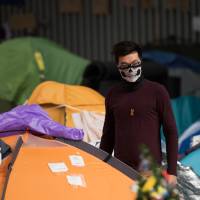 A protester wearing a mask gets out of his tent at the movement\'s main protest site in the Admiralty district of Hong Kong on Saturday. | AFP-JIJI