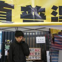 Student protest leader Joshua Wong talks on his phone during his hunger strike at the area occupied by pro-democracy demonstrators outside government headquarters in Hong Kong on Tuesday. The yellow banner above him reads \"Genuine universal suffrage.\" | AP
