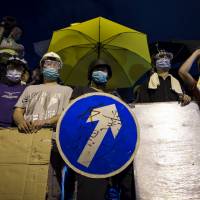 A pro-democracy protester holds a road sign as a shield while standing in front of riot police close to the chief executive’s office in Hong Kong on Nov. 30. | REUTERS