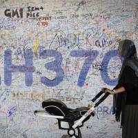 A woman walks past a board displaying messages of hope for passengers aboard missing Malaysia Airlines Flight MH370 at Kuala Lumpur International Airport on March 19. | AP