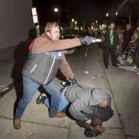 An undercover California Highway Patrol detective, who had been marching with anti-police demonstrators, aims his gun at protesters during an arrest after some in the crowd identified him and his partner (center) in Oakland, California, on Wednesday. | REUTERS