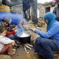 A Syrian refugee with her children prepares food near her tent last December as a heavy snowstorm batters the region, including the camp for Syrians who fled their country\'s civil war in the Chouf mountain town of Ketermaya, Lebanon. The U.N. World Food Program says it has suspended a food voucher program serving more than 1.7 million Syrian refugees because of a funding crisis. The WFP says the program provided Syrian refugees in Jordan, Lebanon, Turkey, Iraq and Egypt with vouchers to buy food in local shops. | AP