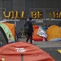 A man walks past protesters\' tents on a main road at the occupied area outside government headquarters in Hong Kong on Wednesday. | AP