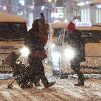Pedestrians cross a street in Sapporo during a snow storm on Monday. | KYODO