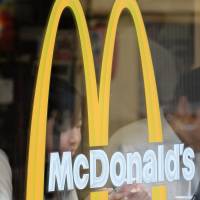 Customers sit behind a logo at a McDonald\'s restaurant in Tokyo in July. | BLOOMBERG