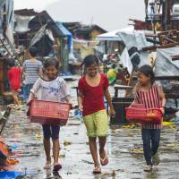 Filipino children carry food and other items on Sunday in Tacloban, the heart of the region devastated by Typhoon Haiyan a year ago, after homes collapsed due to Typhoon Hagupit. The storm knocked out power across entire coastal provinces, mowed down trees and sent more than 650,000 people into shelters before it weakened Sunday. | KYODO