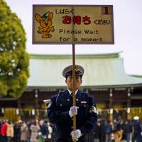 A police officer holds a sign asking visitors to wait as they line up to pray on the first day of the new year at Shinto Meiji Shrine in Tokyo. | REUTERS