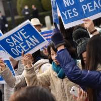 Protesters against the new U.S. Marine base planned for Henoko Bay in Nago, Okinawa, hold placards outside the Diet on Sunday. | FINBAR O\'MALLON