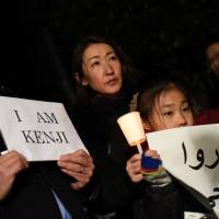 People hold up \"Free Kenji\" signs in English and Arabic calling for the release of Islamic State captive Kenji Goto on Wednesday evening in front of the prime minister\'s office. | FINBAR O\'MALLON