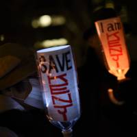 People hold PET bottles fashioned into lamps at a demo calling for the release of Islamic State captive Kenji Goto on Wednesday evening in front of the prime minister\'s office. | FINBAR O\'MALLON
