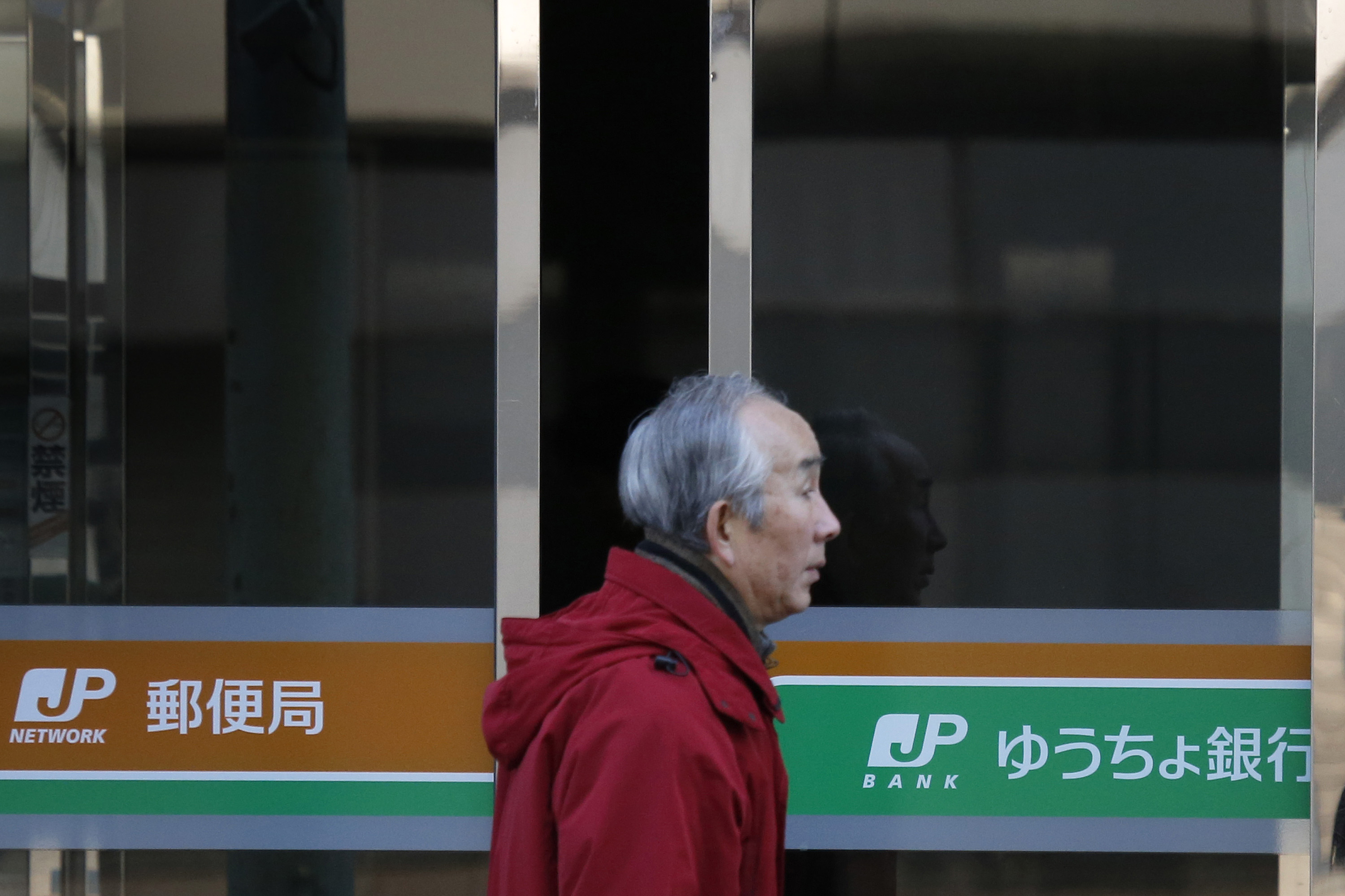 A man walks past a Japan Post and a Japan Post Bank branch in Tokyo in December. | BLOOMBERG