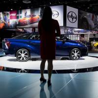 A woman stands next to Toyota\'s new Mirai fuel cell vehicle at the 2015 North American International Auto Show in Detroit on Jan. 13. | BLOOMBERG