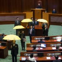 Pro-democracy lawmakers hold yellow umbrellas &#8212; the symbol of the Occupy Central movement &#8212; as Chief Executive Leung Chun-ying (center) delivers his annual policy address at the Legislative Council in Hong Kong on Wednesday. | REUTERS