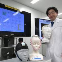 Ryohei Hasegawa, who leads a neurotechnology group at the National Institute of Advanced Industrial Science and Technology, poses with the Neurocommunicator on Dec. 4 in Ibaraki Prefecture. | KAZUAKI NAGATA