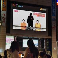 People watch a large TV screen in Tokyo on Tuesday showing news reports about the two Japanese men (kneeling) being held by the Islamic State group. | AFP-JIJI